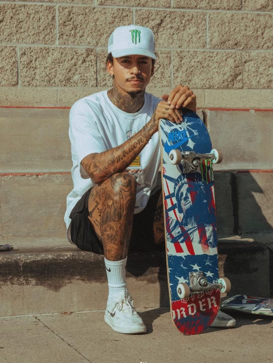 Nyjah Huston sentado com seu Skate em uma calçada