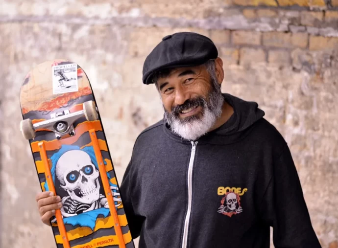 Steve Caballero sorrindo para a câmera com seu skate na mão