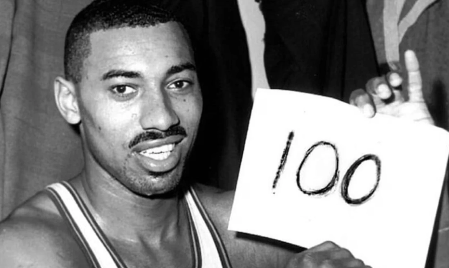 Wilt Chamberlain segurando uma placa com o número "100", que indica seu recorde na NBA